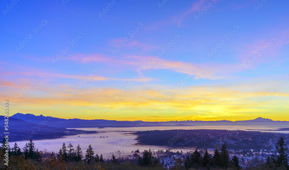 Sunrise over Fraser Valley, BC, Canada, with the tips of high-rise buildings just visible through dense cloud inversion covering much of the valley floor.