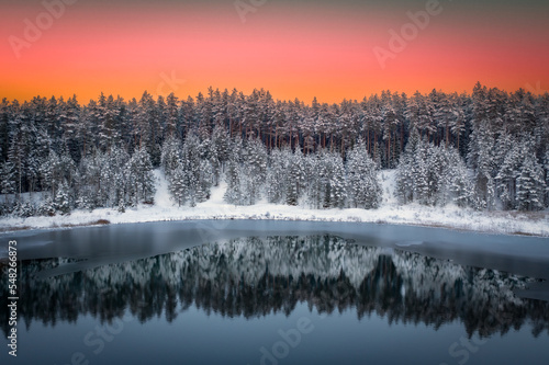 Colorful landscape with snowy trees and reflection at sunset time on the lake