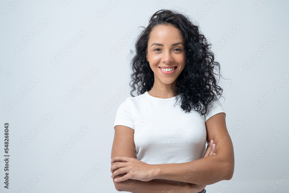 Obraz premium Portrait of smiling latin woman with curly hair with crossed arms isolated on grey background.