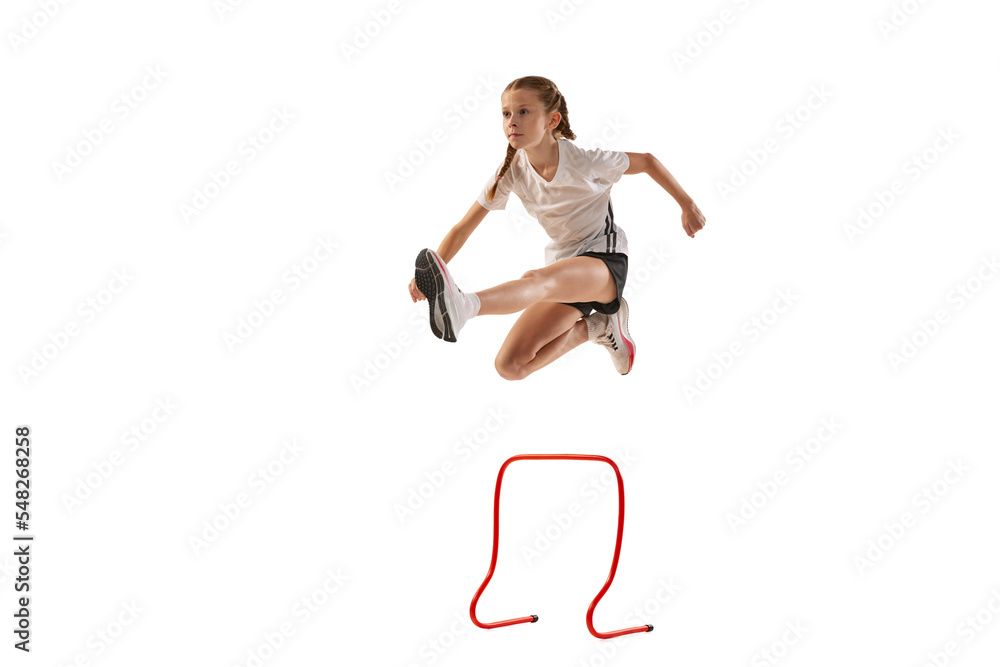 Dynamic portrait of little girl, professional athlete, runner, jogger at steeplechase training isolated over white background