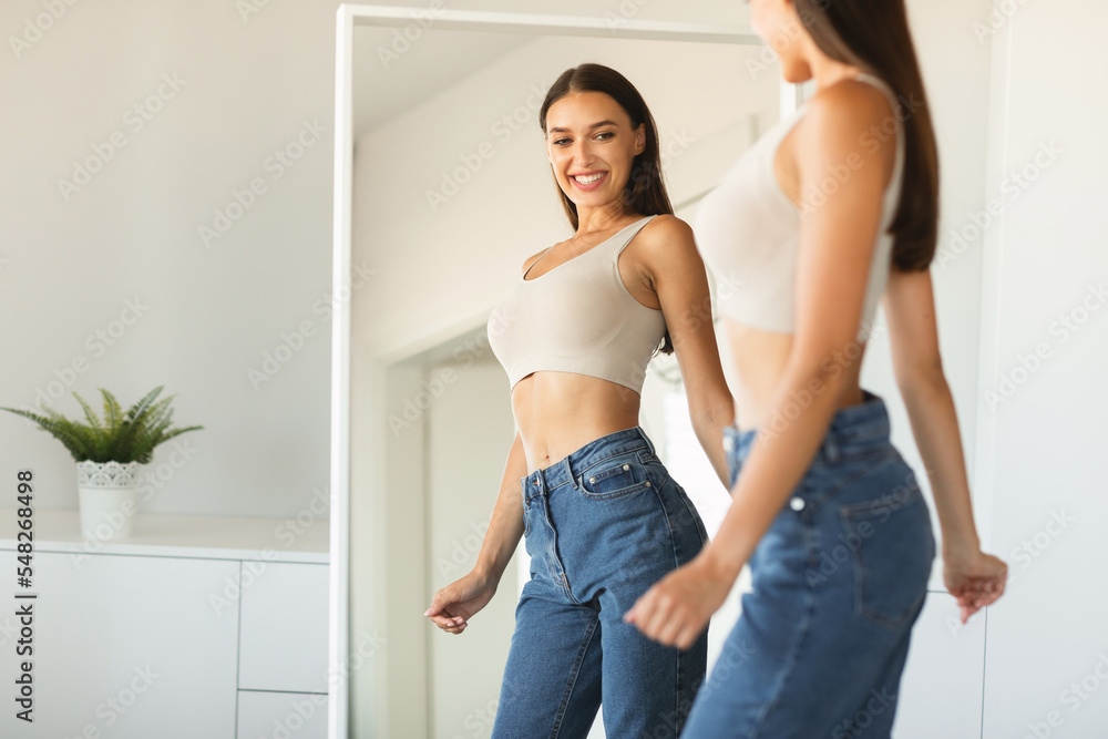 Happy caucasian lady enjoying her reflection in mirror, posing after successful weight loss near mirror Happy caucasian lady enjoying her reflection in mirror, posing after successful weight loss near mirror