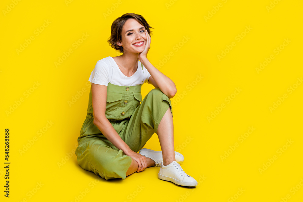 Full size photo of cute young girl sit floor relaxed listen interesting story wear trendy khaki clothes isolated on yellow color background Full size photo of cute young girl sit floor relaxed listen interesting story wear trendy khaki clothes isolated on yellow color background