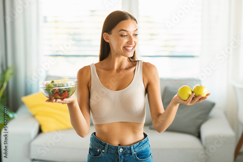 Happy young woman holding salad in bowl and apples, enjoying and recommending weight loss nutrition