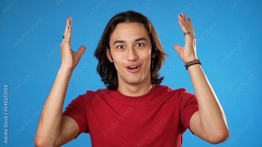 Handsome thinking gender fluid young man 20s, looks at camera gives mind blown gesture showing explosion of ideas posing on blue background. Handsome thinking gender fluid young man 20s, looks at camera gives mind blown gesture showing explosion of ideas posing on blue background.