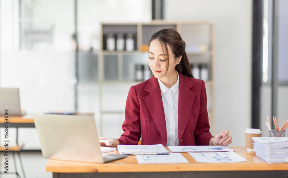 Asian woman working laptop in workplace, Business woman wearing red jacket suit busy working on laptop computer checking finances, investment, economy, saving money or insurance concept Asian woman working laptop in workplace, Business woman wearing red jacket suit busy working on laptop computer checking finances, investment, economy, saving money or insurance concept