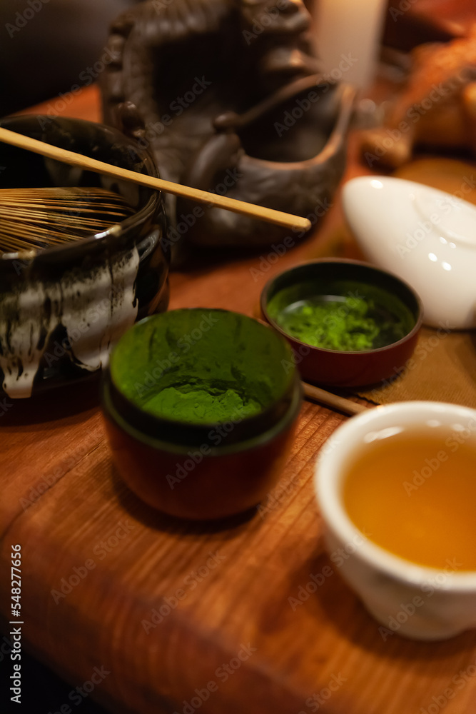 Blurred background - japanese tea party, close-up of objects for the ceremony on a wooden table, matcha green ground tea, tea whisk, cup of tea, cozy atmosphere by candlelight Blurred background - japanese tea party, close-up of objects for the ceremony on a wooden table, matcha green ground tea, tea whisk, cup of tea, cozy atmosphere by candlelight