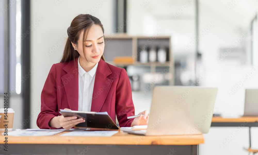 Asian Businesswoman Using laptop computer and working at office with calculator document on desk, doing planning analyzing the financial report, business plan investment, finance analysis concept. Asian Businesswoman Using laptop computer and working at office with calculator document on desk, doing planning analyzing the financial report, business plan investment, finance analysis concept.