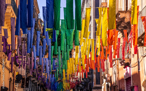 european street, decorated with hanged colorful ribbons in lgbt flag colors, city art with symbol of peace