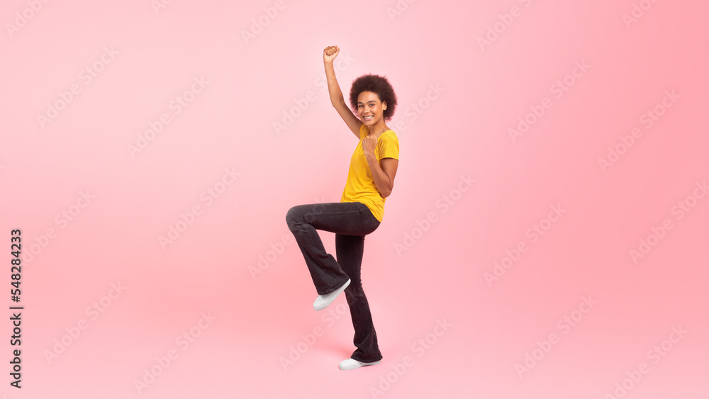 Happy millennial african american curly woman student in casual rejoices, makes gesture of victory and success