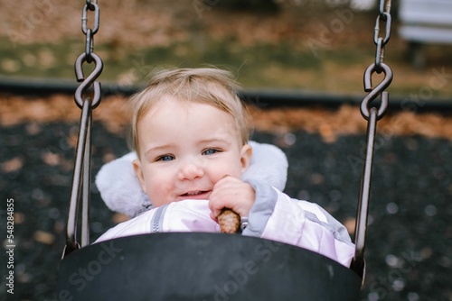 Closeup of a cute 1-year-old girl on a swing holding a pinecone. Morris Plains, NJ, November.