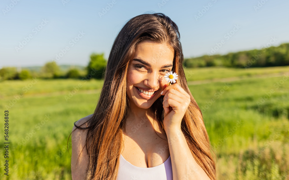 Gorgeous young woman holding a tiny flower outdoors. Happy young woman holding a tiny flower outdoors and smiling.