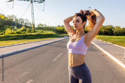 Hispanic women getting ready for her run. Young happy muscular build woman tying up her hair while preparing for running in nature. Copy space.