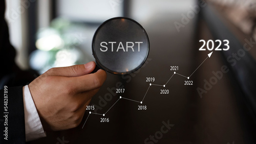 Businessman holding a magnifying glass and the word new start in 2023