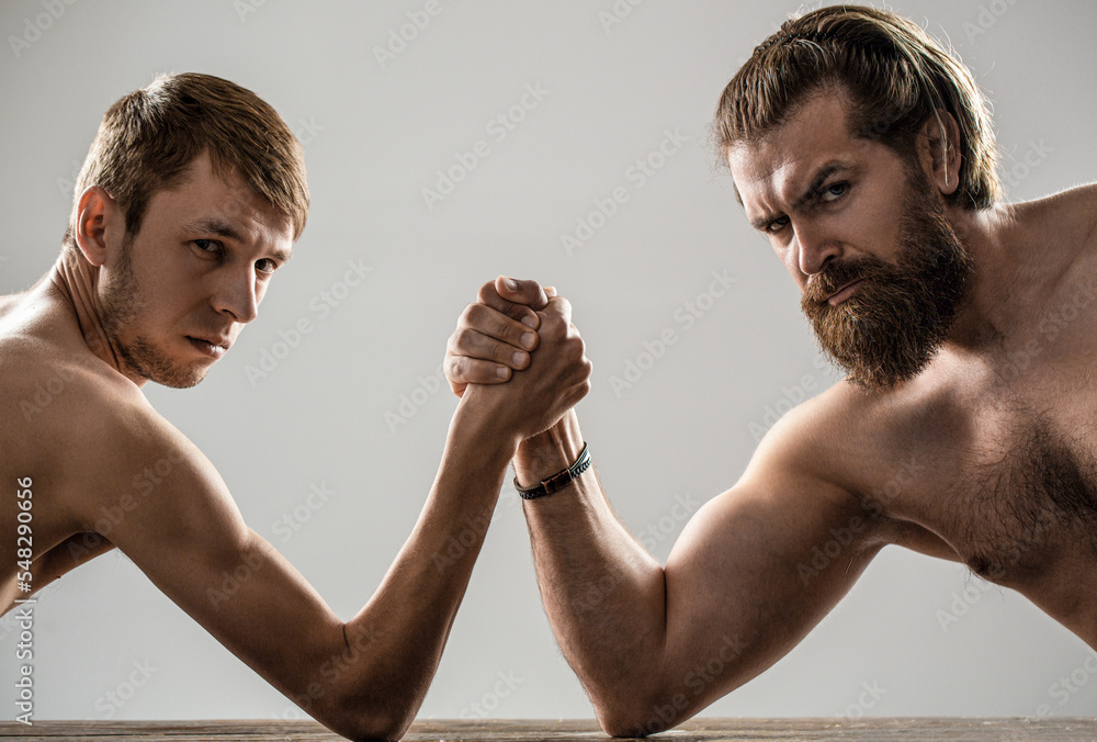 Arm wrestling. Heavily muscled bearded man arm wrestling a puny weak