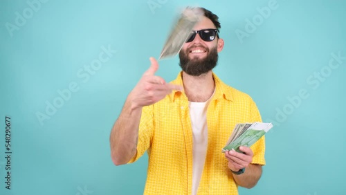 Bearded man throwing money around with a smile, showing off a rich life, the concept of careless spending money. Indoor studio shot on a blue background.