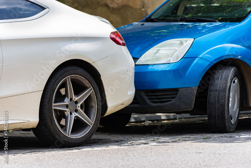 White luxurious car parked in front of a blue vehicle with a small space to get out of parking