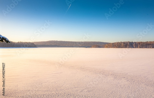 Winter landscape with snow-covered forest, river on a blue sky background