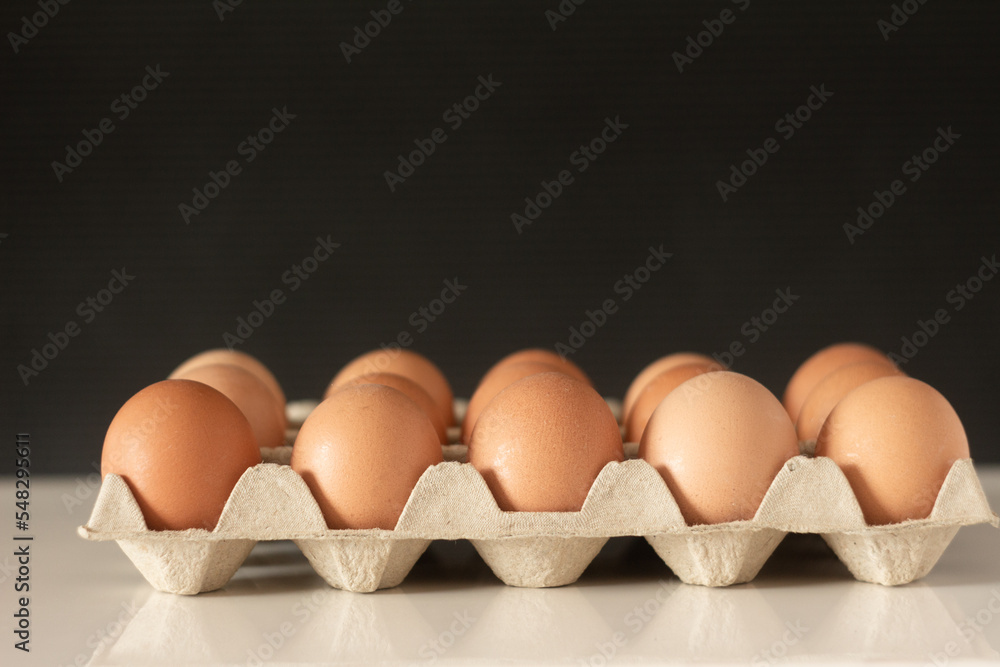 a tray of eggs - a lot of brown eggs in a cardboard stand - on a white table and with a dark background a tray of eggs - a lot of brown eggs in a cardboard stand - on a white table and with a dark background
