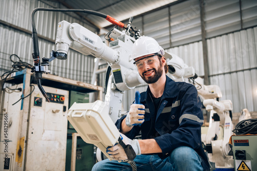 Happy caucasian man specialist engineer holding robotic arm controller in welding machine factory. Technician automation robot team in blue uniform working in robot industry