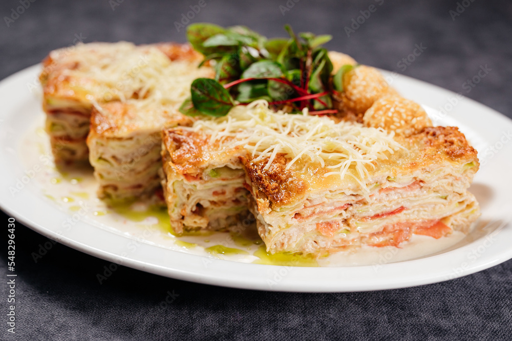 Fried cheese balls, and potato lasagna, on a white plate, decorated with herbs and cheese. Concept of restaurant, food.