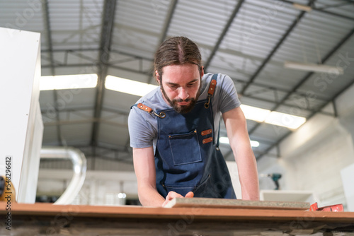 A furniture workshop making bespoke contemporary furniture pieces using traditional skills in modern design. A man in ear defenders holding wood  using a machine.