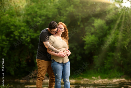 Female holding same sex partners pregnant stomach outdoors.
