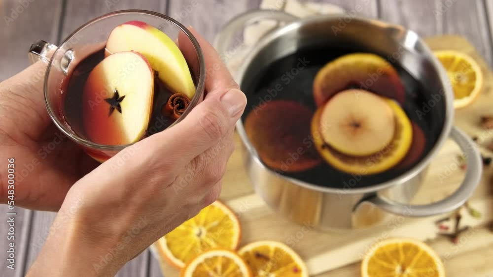 Woman's hands holding a glass mug with mulled wine, closeup 4k video, Christmas punch, festive alcohol drink, scented red hot wine with cinnamon, orange, apple fruit and spice, hd footage Woman's hands holding a glass mug with mulled wine, closeup 4k video, Christmas punch, festive alcohol drink, scented red hot wine with cinnamon, orange, apple fruit and spice, hd footage