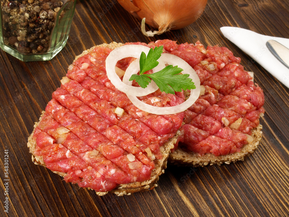 Spicy Beef Tartar Meat on a Bread Roll with Onions on wooden Background Spicy Beef Tartar Meat on a Bread Roll with Onions on wooden Background