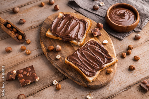 Board of bread with chocolate paste and hazelnuts on wooden background