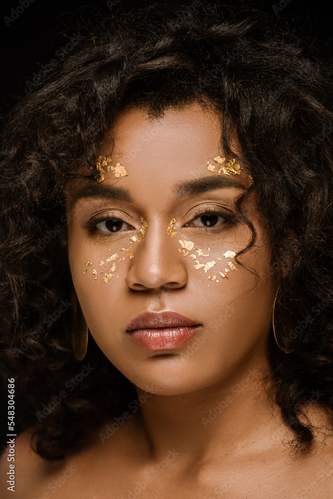 brunette african american woman with golden body paint on cheeks isolated on black.