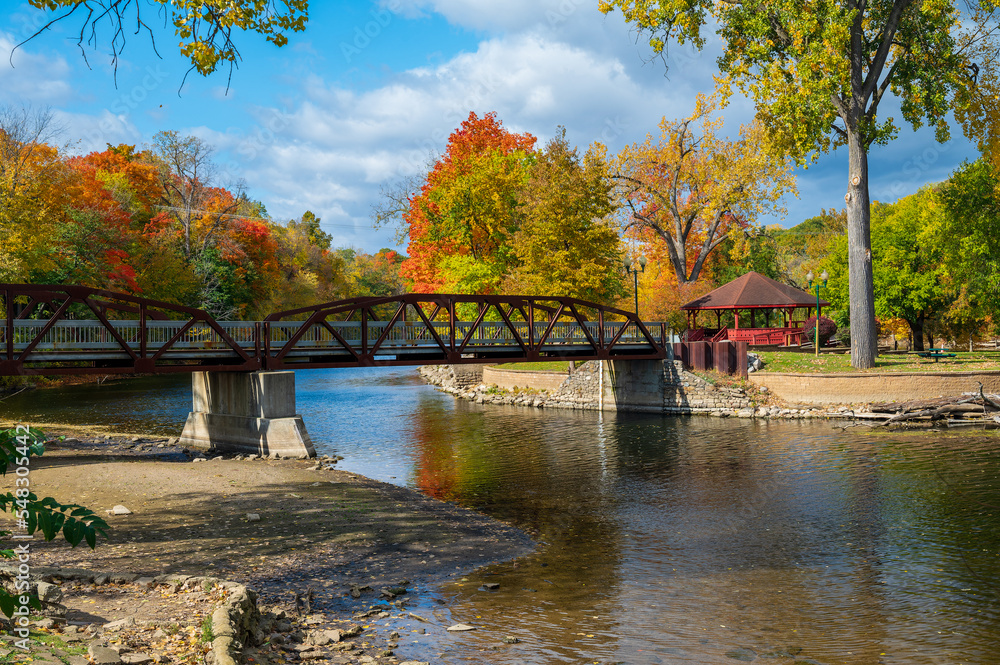 Fototapeta premium Vibrant fall colors surrounding the bridge in Island Park Grand Ledge, MI