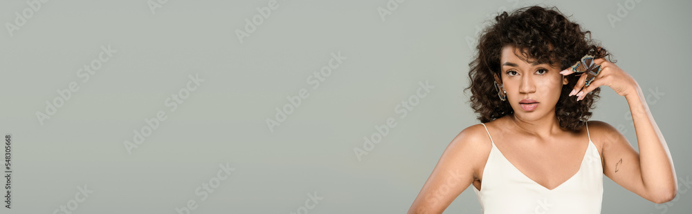 pretty african american woman with butterflies on hand and face posing isolated on grey, banner. pretty african american woman with butterflies on hand and face posing isolated on grey, banner.