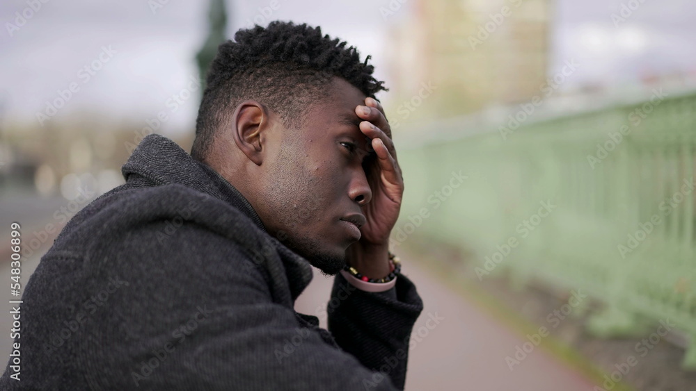 Preoccupied black African man sitting at city street curb feeling anxiety4 Preoccupied black African man sitting at city street curb feeling anxiety4