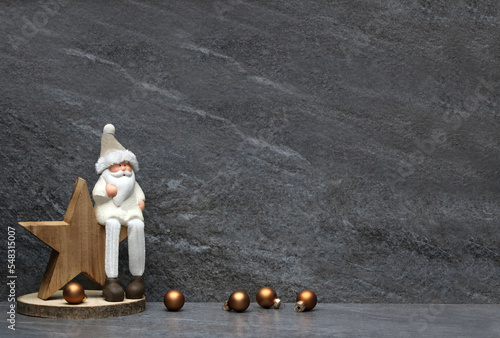 Weihnachtsmann mit Stern und Weihnachtskugeln vor einer Marmorwand nit Platz für Text.