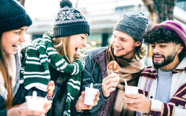 Happy friends having fun eating sweets at Christmas market on winter time - Vintage holiday concept with young people hanging out together by candy shop wearing warm trendy cloth - Bright azure filter