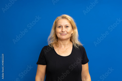 Portrait of a pretty caucasian lady in her 40s dressed in a black t-shirt isolated over blue studio background. © Andres