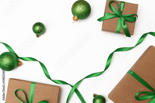 Flat lay of craft present boxes with green ribbons and christmas balls on the white background