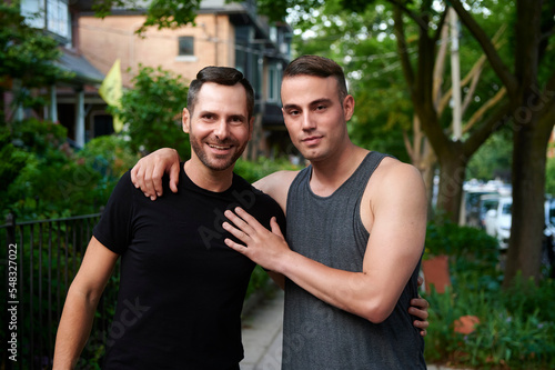Same sex male couple with arms around each other outdoors.