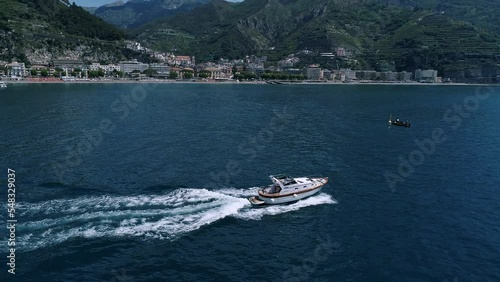 Aerial view of a boat on the Amalfi Coast, Italy. Drone slow motion footage with smooth camera movement. Sea waves diverge from the movement of the yacht on a sunny day