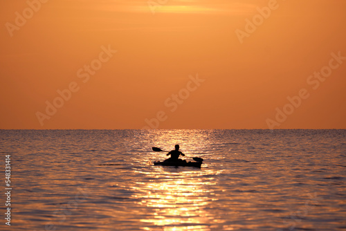 Dark figure of sportsman rowing alone on his kayak boat on sea water at sunset. Active extreme sports concept © bilanol