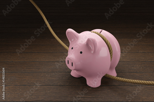 Foto Pink piggy bank is tightened by a rope on wooden table