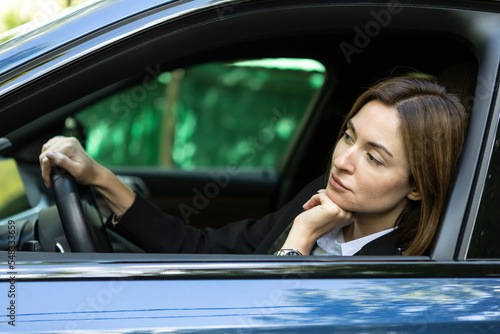 Nervous business woman driving and peeps out of the window of her luxury car. Discontented woman in black suit standing in traffic jam and looking out of her car and demonstrating her displeasure © Vitaliy