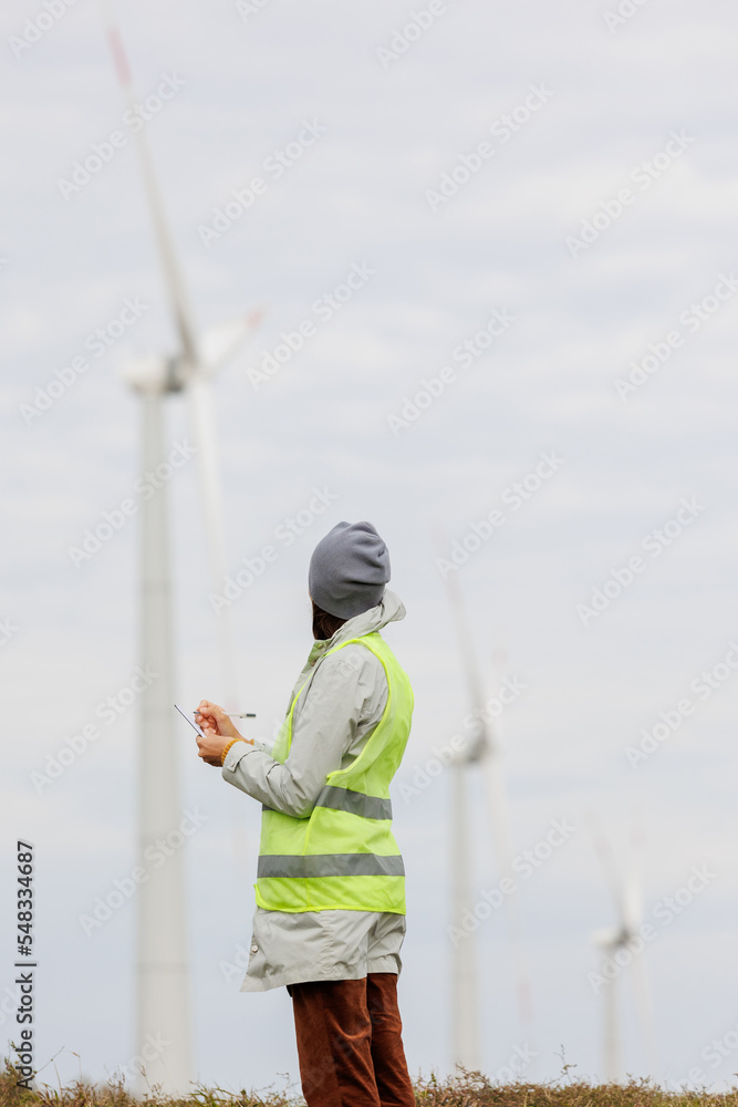 female engineer in a protective vest takes measurements of the speed of wind turbines. electricity is generated by wind. technologies without an eco trace. engineering solution. generating electricity female engineer in a protective vest takes measurements of the speed of wind turbines. electricity is generated by wind. technologies without an eco trace. engineering solution. generating electricity