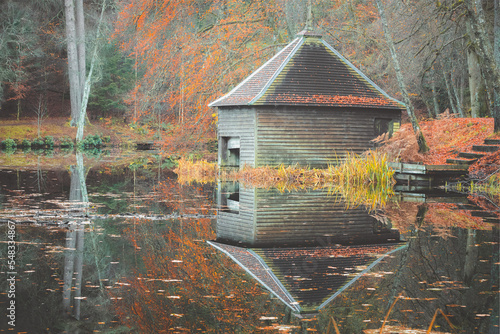 A colourful autuman woodland scene of an old abandoned boathouse over a calm still lake reflection on Loch Dunmore at Faskally Forest in Perth and Kinross, Scotland. photo