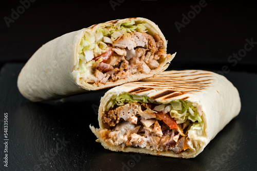 Fresh shawarma from chicken, tomatoes, lettuce, herbs, sauce and pita bread on a dark background.