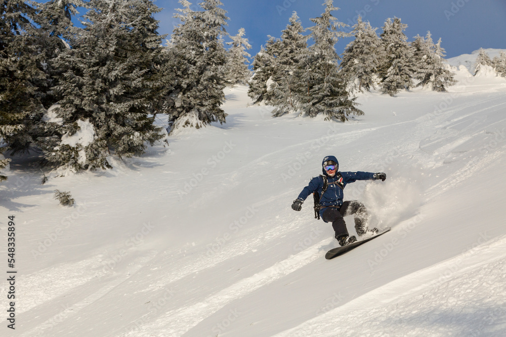 An active man rides on a snowboard freeriding on a snowy slope in a backcountry alpine terrain in the Carpathians mountains