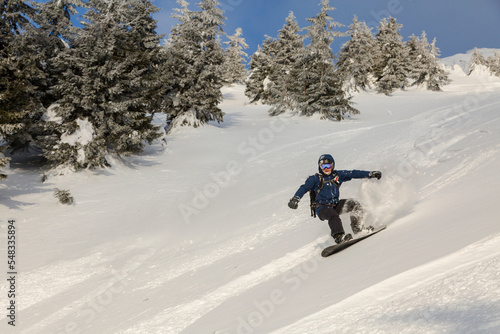 An active man rides on a snowboard freeriding on a snowy slope in a backcountry alpine terrain in the Carpathians mountains