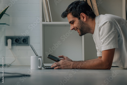 young man at home with mobile phone and laptop on the floor