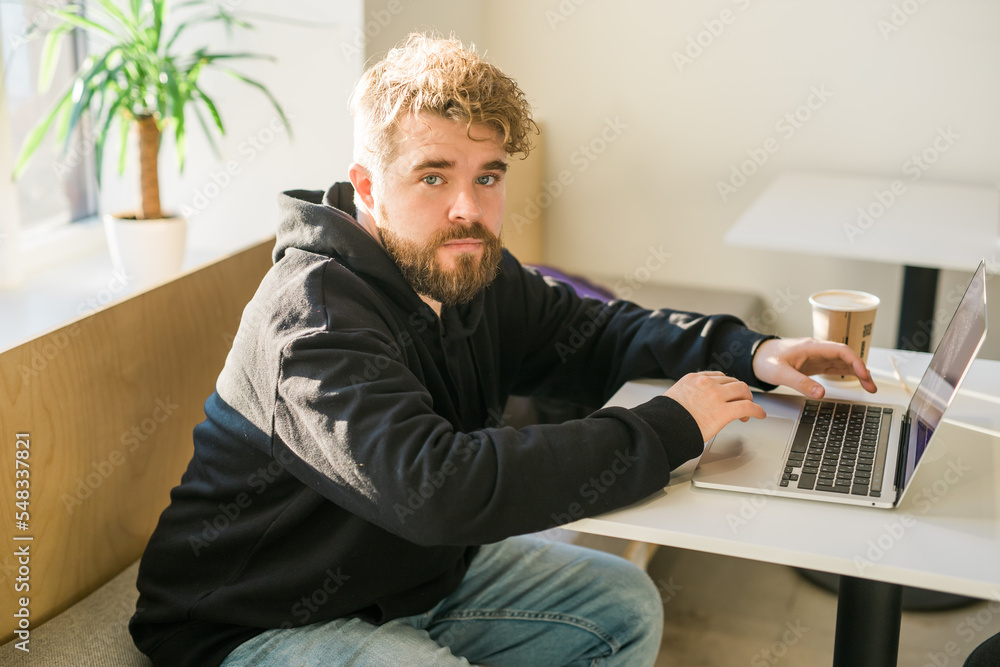 Male guy resting in coffee shop chatting in social networks skilled freelancer enjoying remote job typing publication for web blog on laptop