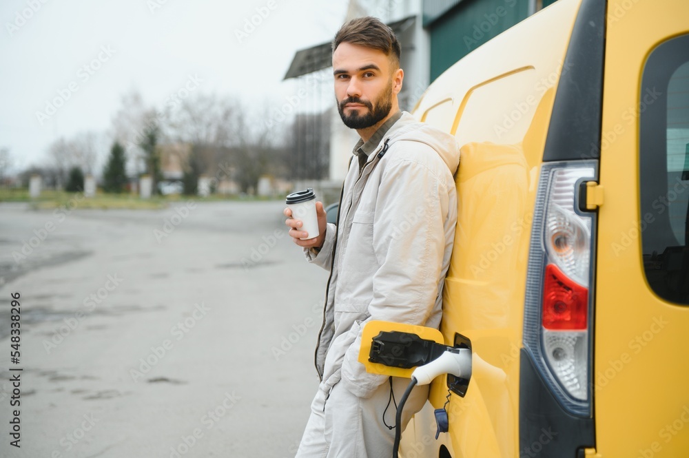 Casual man near electric car waiting for the finish of the battery charging process Casual man near electric car waiting for the finish of the battery charging process